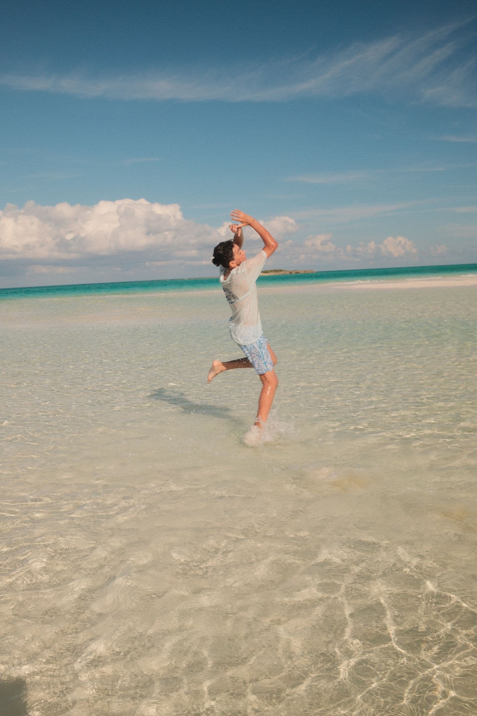 Boy leaping in turquoise water, arms raised