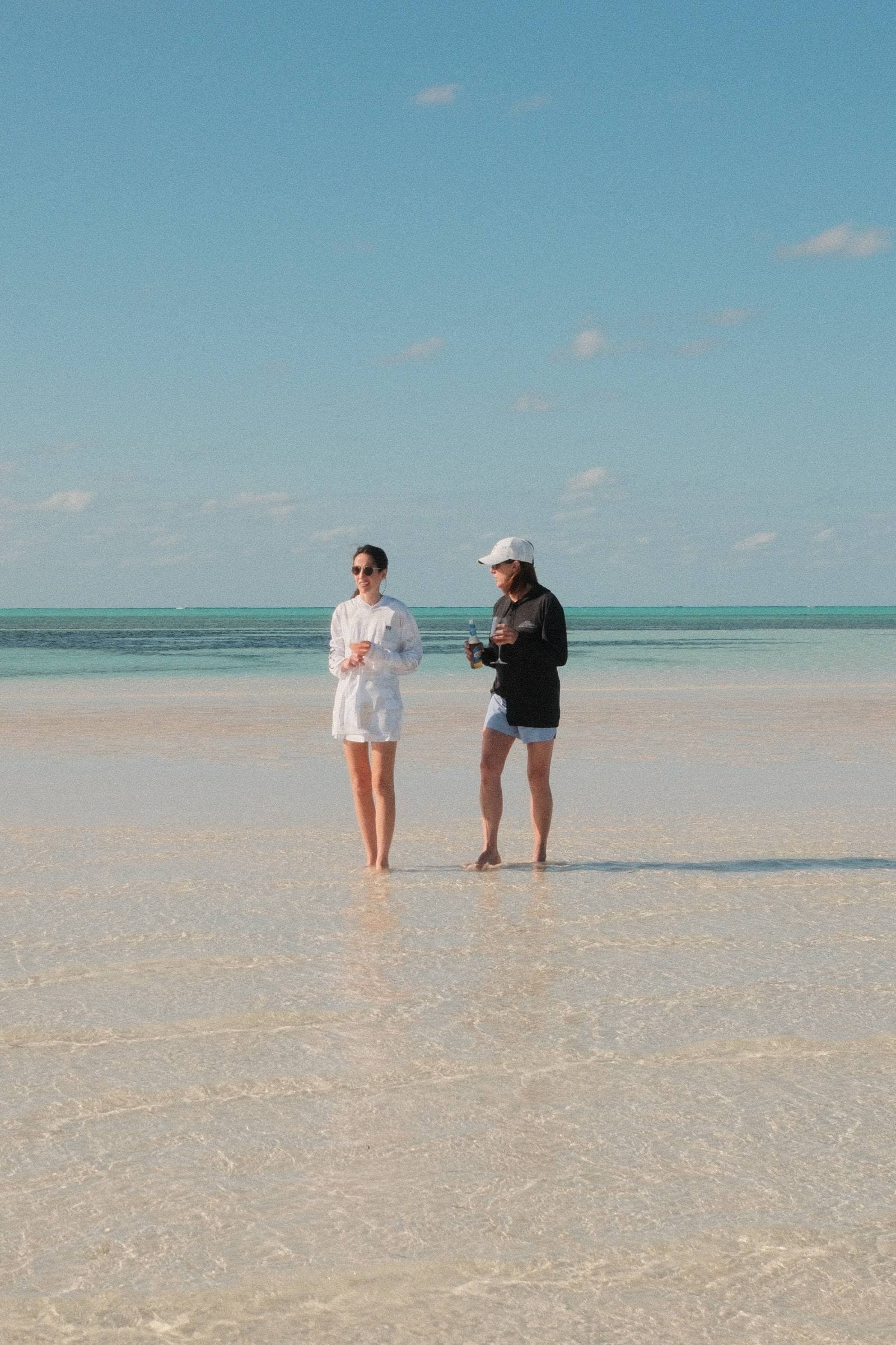 Two women on vast sandbar sharing drinks