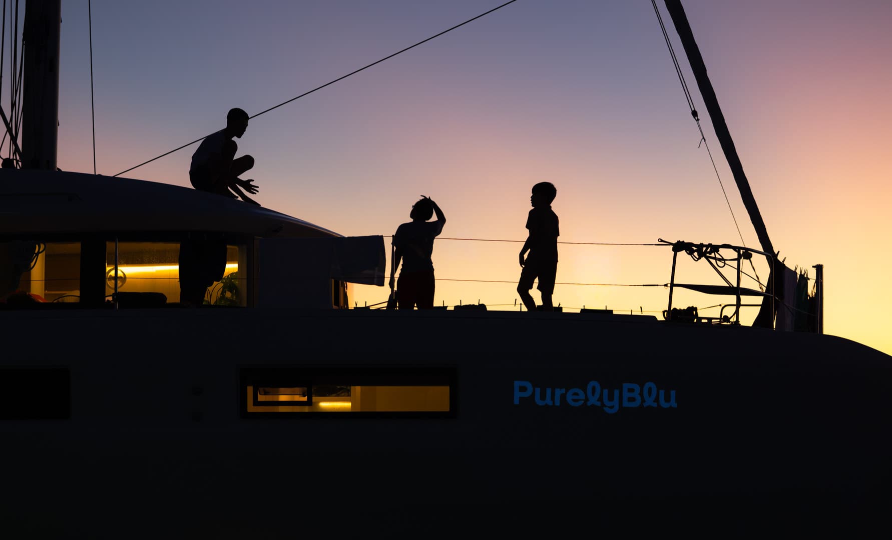 Guests on deck at dusk with PurelyBlu's cabin lights glowing through the windows
