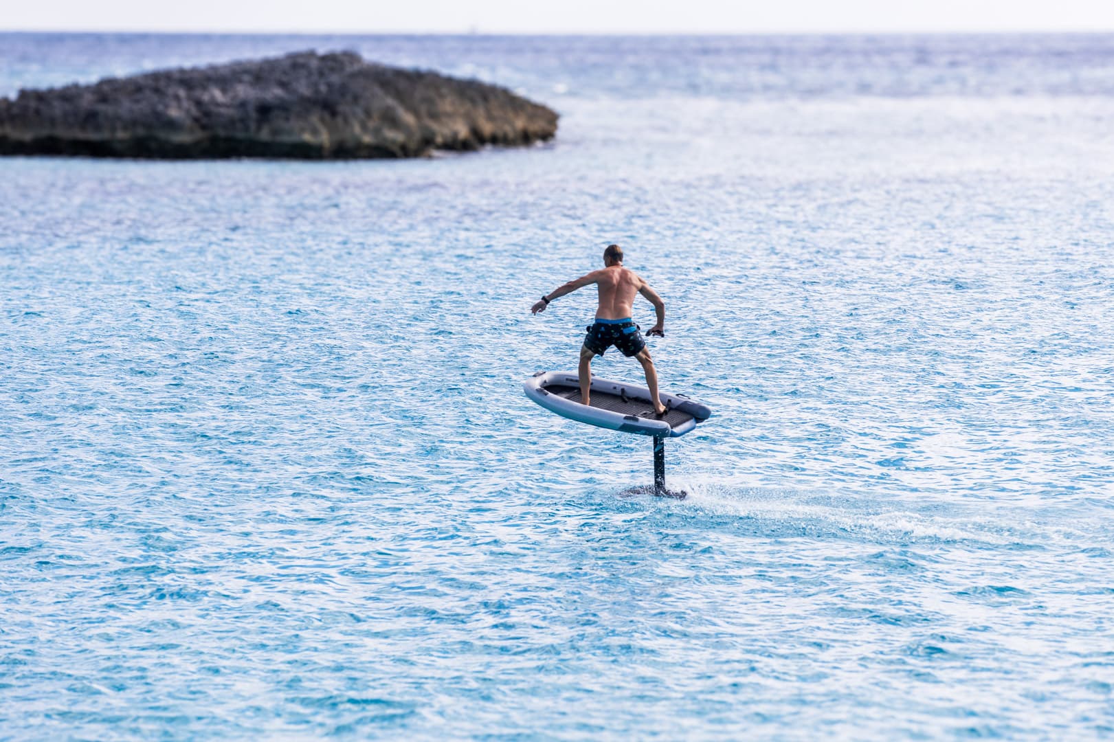 Rider foiling above the water on an eFoil beside a rocky Exumas cay