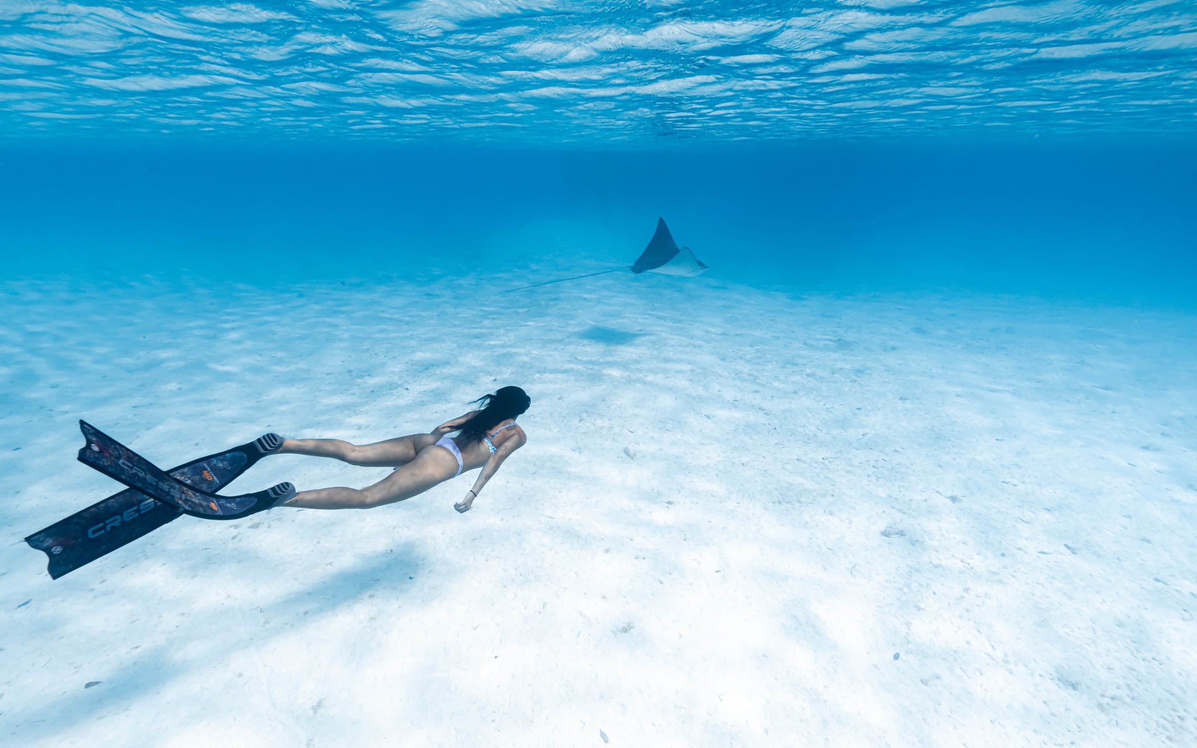 Freediver toward stingray on white sand